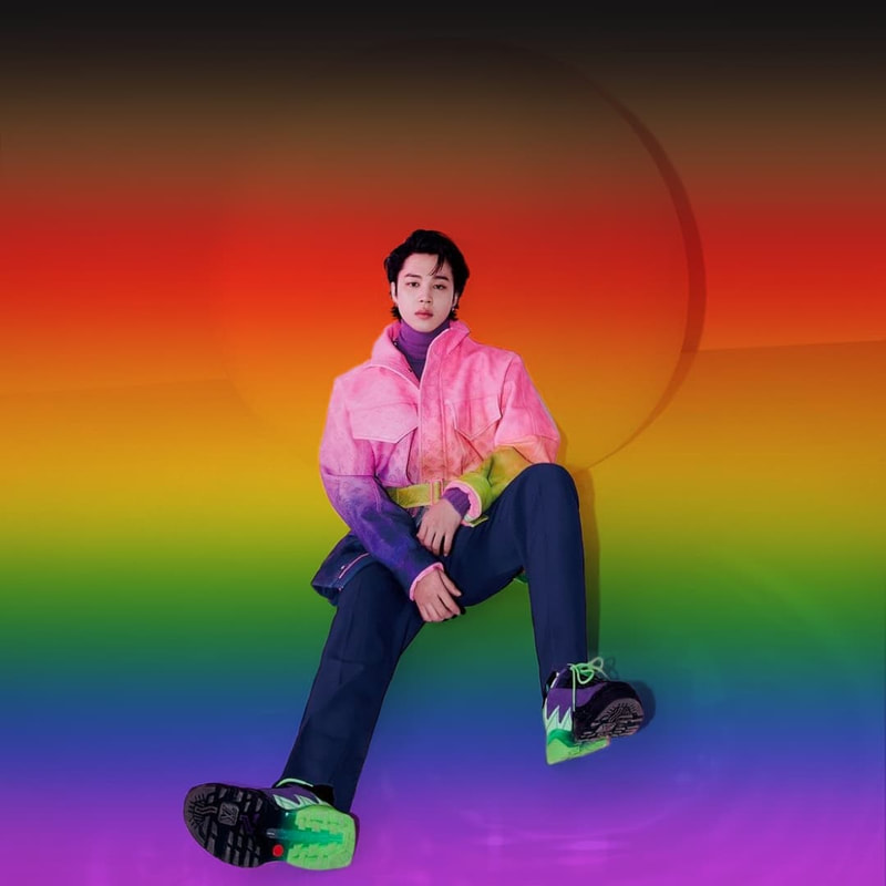 photo of jimin from gq x vogue photoshoot where he's leaning on a big sphere. the entire photo background, including the sphere he is leaning on, is a blurred philly rainbow flag except jimin. 