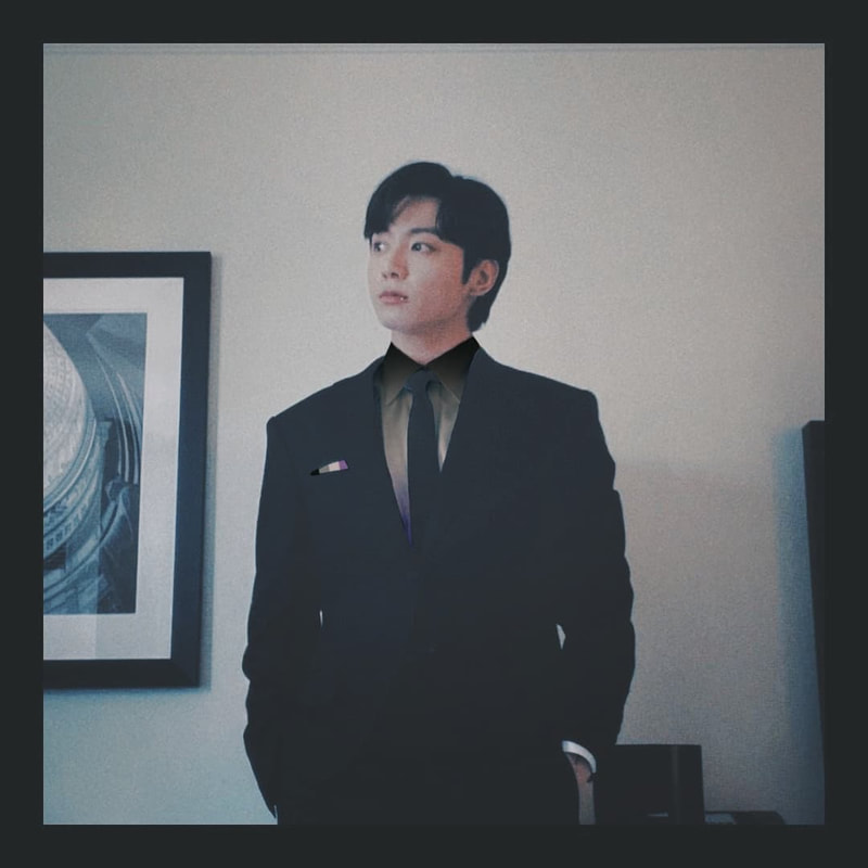 instagram post photo of jungkook in a suit with a vintage style filter on May 31st, 2022. His dress shirt peaking out from underneath his suit is blurred vintage style asexual flag colored and he has a pocket square peaking out that is a vertically placed vintage asexual flag.