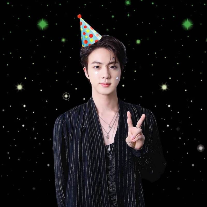 Cutout of Seokjin in a black dress shirt with thin vertical stripes on it and stars on his cheeks giving a peace sign with a tilted light blue cartoon birthday hat on his head that has red dots, yellow stars, and a small red pom pom on it. The background is a black galaxy with stars that is blurred aromantic flag colored. 